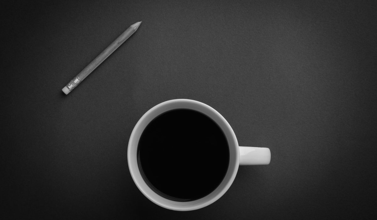 En kop sort kaffe og en blyant på et mørkt bord, set ovenfra