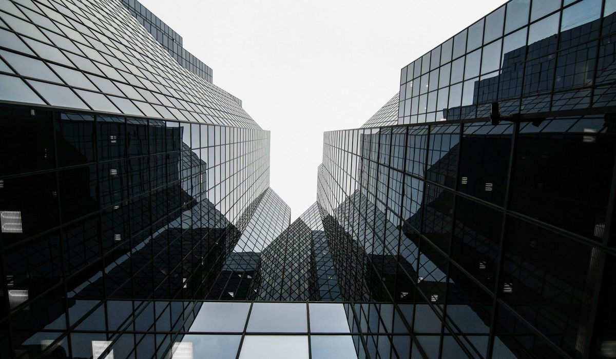 To glasfacader set nedefra, der spejler hinanden mod en hvid himmel